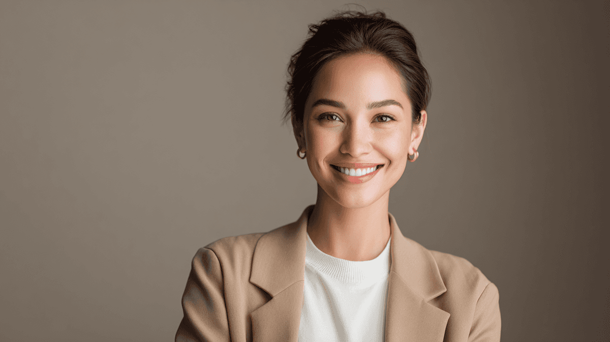 Smiling young professional woman in a beige blazer with a clean studio background.